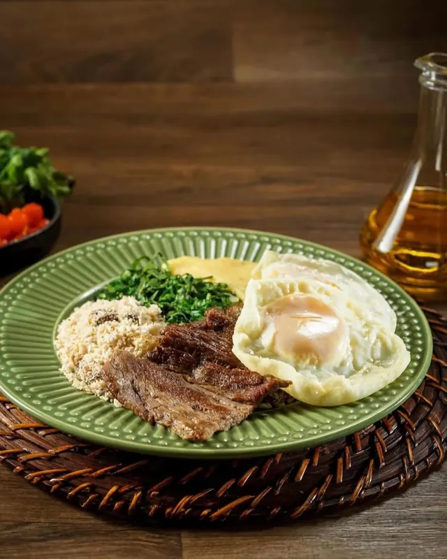 Bife a cavalo com ovos fritos no prato verde, com couve, farofa e angu